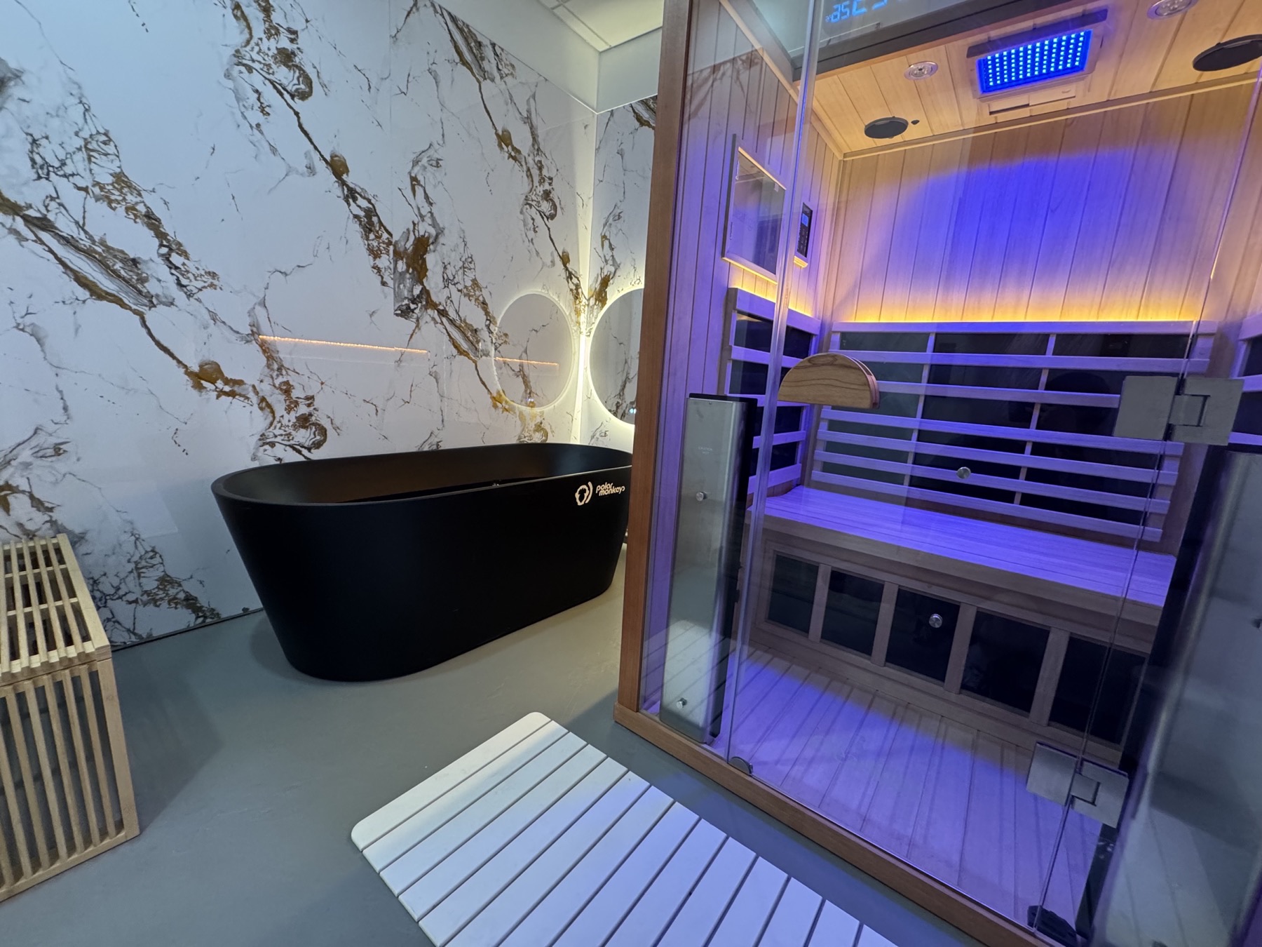 A private Sauna House suite with a black cold plunge tub beside a cedar infrared sauna cabin